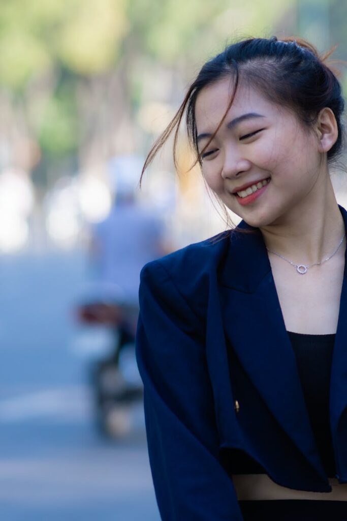 Young woman in navy clothing smiling outdoors on a city street during the day.